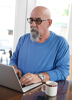 Hombre sentado en la mesa de la cocina trabajando con una computadora portátil.